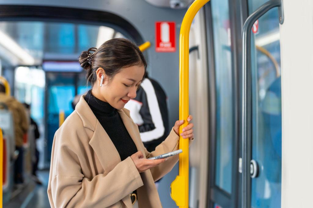 A woman using mobile phone and listening to the music on earphones during travel on train in Sydney city.