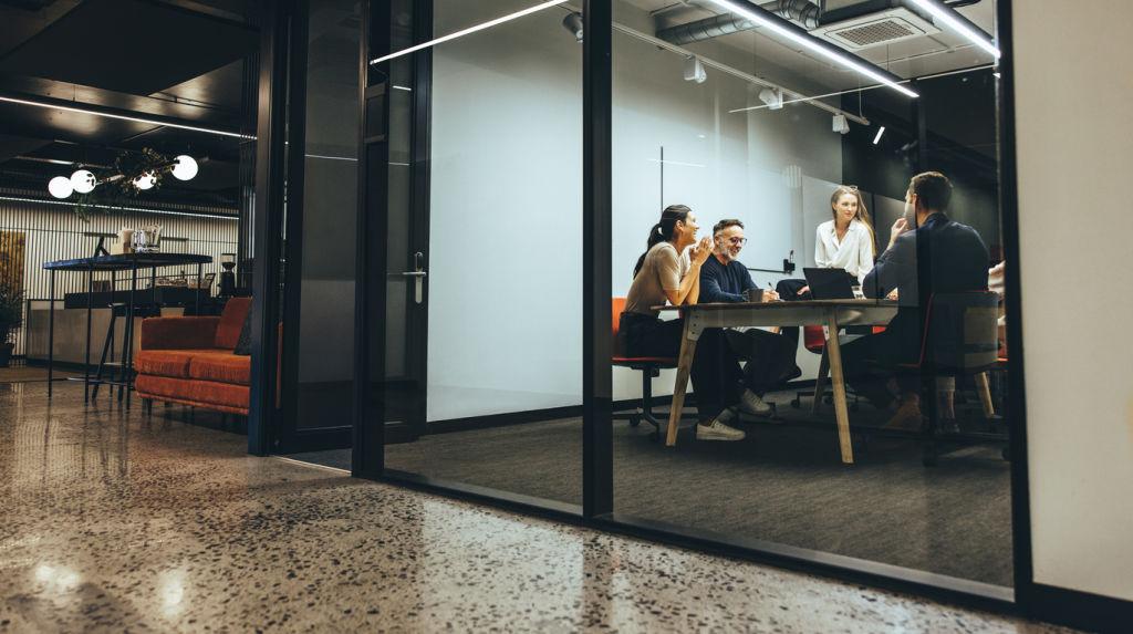 Business colleagues having a meeting in a transparent boardroom. Group of happy business professionals having a discussion during a briefing. Diverse businesspeople collaborating on a new project.